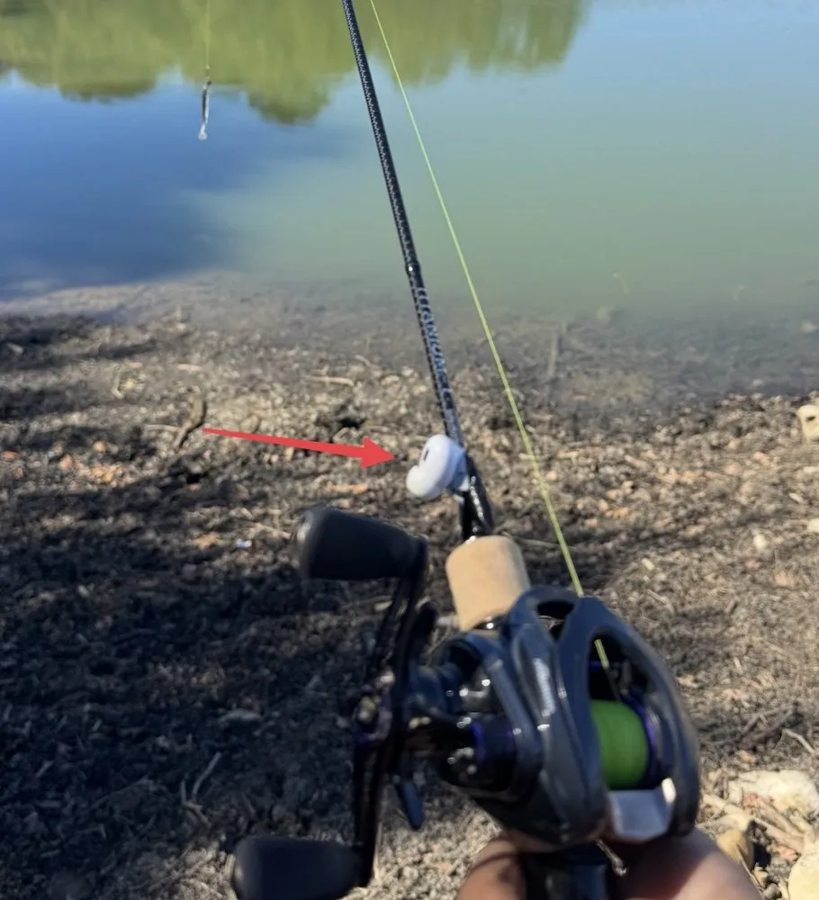 A white AirPod taped to the blank of a casting rod just ahead of the cork grip, on the side away from the line. A red arrow points to it.